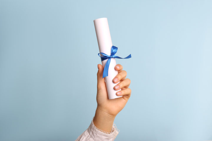 Student holding rolled diploma with ribbon on light blue background, closeup